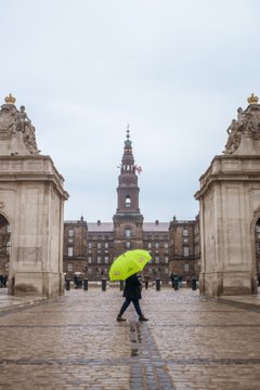 A Copenhagen Free Walking Tours tour guide carrying a green umbrella in front of Christiansborg Palace