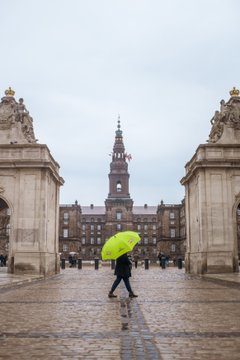 A Copenhagen Free Walking Tours tour guide carrying a green umbrella in front of Christiansborg Palace